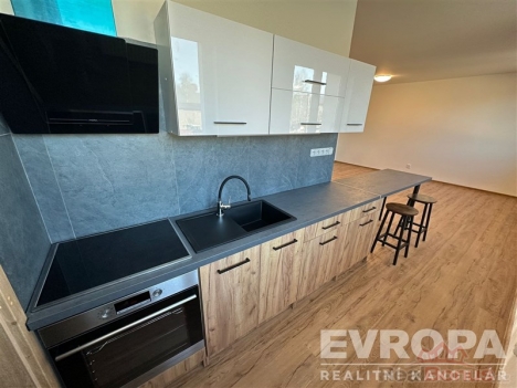 Modern� kuchy� s parketovou podlahou, d�ev�n�mi sk���kami a �ern�mi spot�ebi�i, vedle prostoru pro j�deln� st�l �i barov� pult