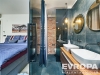 Modern� koupelna s tmav�mi obklady, dvojit�m umyvadlem a zrcadly, cihlov� st�na v pozad� p�id�v� industri�ln� �arm.