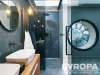 Modern� koupelna s tmavou dla�bou, velk�m kulat�m oknem a sprchov�m koutem. Stylov� design a elegantn� umyvadlo na d�ev�n� desce.