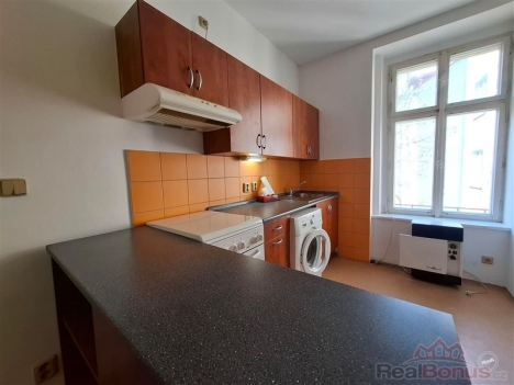 Kompaktn� kuchy� s oran�ov�m obkladem, vestav�n�mi sk��n�mi a lamin�tovou pracovn� deskou, sv�tl� d�ky velk�mu oknu.
