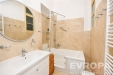 Koupelna s modern� keramickou dla�bou, velk�m kulat�m zrcadlem, vanou se sprchovou z�st�nou a b�l�m umyvadlem na sk���ce.