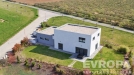 Modern� rodinn� d�m s plochou st�echou, velk�mi okny a betonovou terasou, obklopen� upravenou zahradou na klidn�m p�edm�st�.